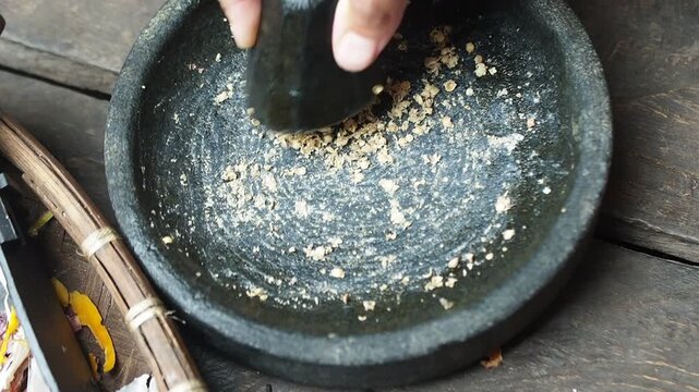 Close-up of a hand grinding dried spices with a stone mortar and pestle on a rustic wooden table, traditional cooking preparation.