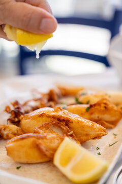 Hand squeezing fresh lemon juice over fried calamari squid in a Greek tavern