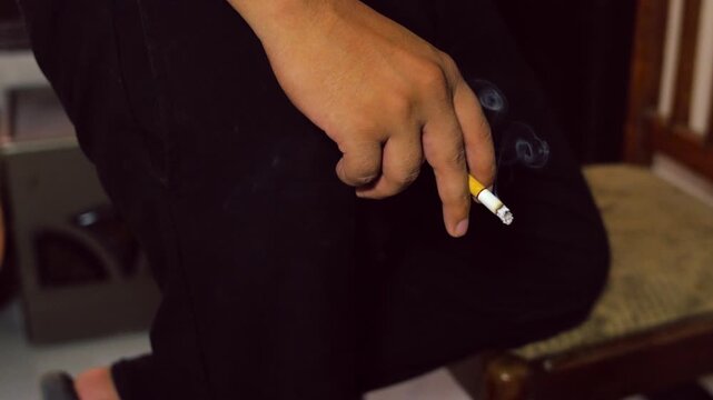 Hand holding a smoldering cigarette in front of dark clothing smoking tobacco nicotine addiction habit smoking tobacco nicotine