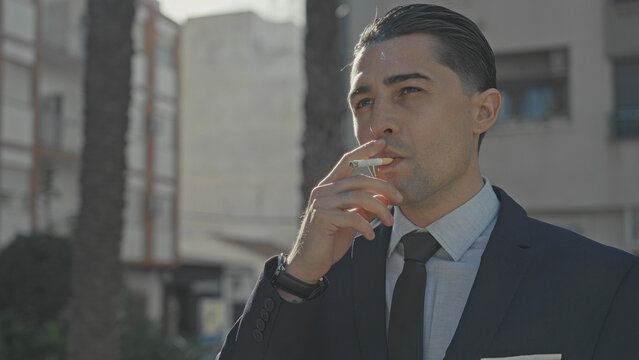 Man in suit smoking a cigarette on street, hand to mouth and exhaling smoke; contemplation solitude reflection.