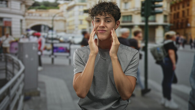 Teen boy touching cheek with hand, grimacing while standing on a busy street with passersby; awkward introspection.