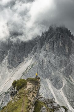 Woman in yellow jacket standing on a ridge, behind her mountain peaks and sharp rocky peaks, dramatic clouds, Cimon the Croda Liscia and Cadini group, Auronzo di Cadore, Belluno, Italy