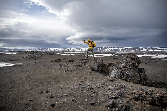 Hiker jumps into the air, snow-covered volcanic landscape with volcanic sand and petrified lava, crater of Askja volcano, Icelandic highlands, Iceland
