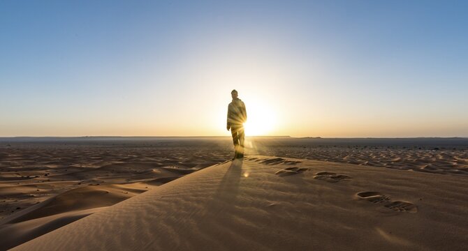 Young man standing on sand dune, sunbeams at sunrise, Erg Chebbi, Merzouga, Sahara, Morocco