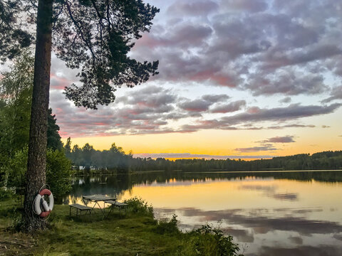 A calm lake at sunset with cloud reflection and trees and red white lifebuoy in the foreground, H&auml;llefors, &Ouml;rebro, Sweden