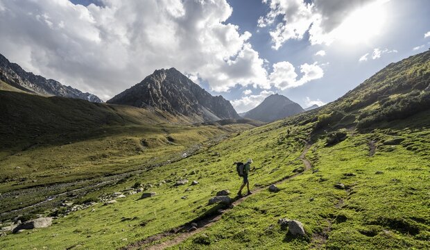 Mountaineers on a hiking trail, green high valley with mountain stream, Keldike Valley on the way to the Ala Kul Pass, Tien Shan Mountains, Kyrgyzstan
