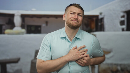 Fototapeta premium Man clutching chest and grimacing at building entrance outdoors, hands pressing over sternum in visible pain; medical emergency pain.