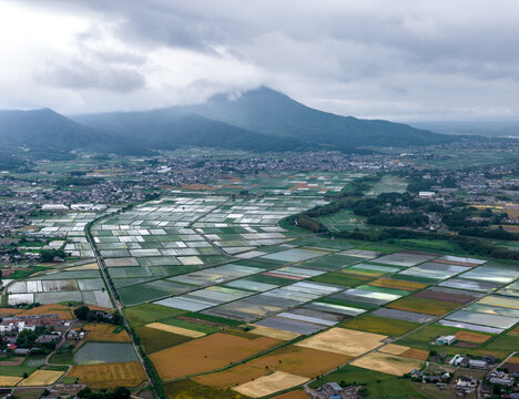 Aerial view of Iwase Rice fields with patchwork patterns of flooded paddies and golden crops, nestled near a town at the base of a mountain in Iwase, Ibaraki, Japan.