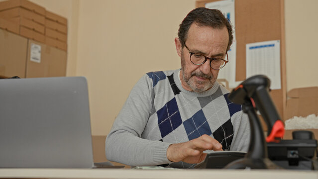 Man counting dollars at laptop with hand on forehead in parcel office building; financial frustration.