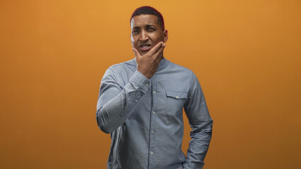 Fototapeta premium Young black man in blue button shirt touching forehead with hand in studio orange backdrop while later frames show him stroking chin; contemplation thought.