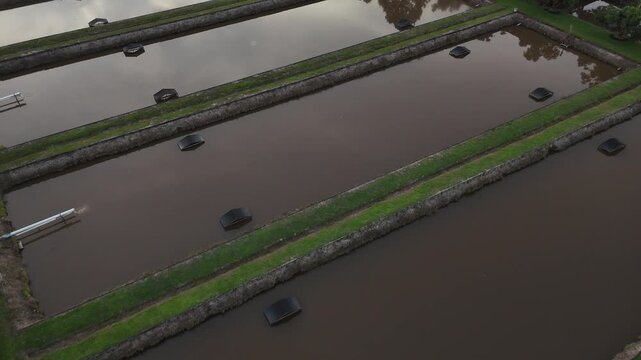 A view from above a rectangular fish farm pond equipped with drainage pipes and embankments.