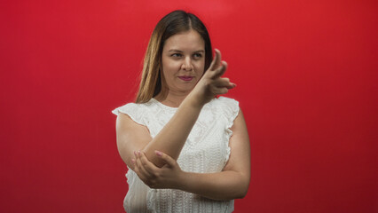 Obraz premium Woman pointing two fingers while holding her forearm in studio with red backdrop; confidence and poise.