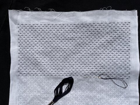 Traditional Japanese Sashiko embroidery in progress on white cotton fabric with dark blue thread and needle, featuring intricate geometric stitching patterns, thread, 
