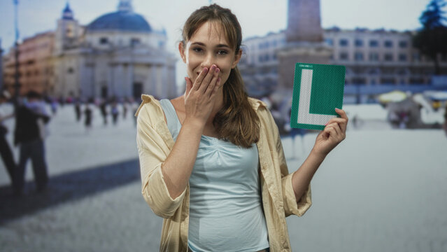 Woman holds green learner l sign, bare shoulder visible at building in st peter's square; confidence learning travel.