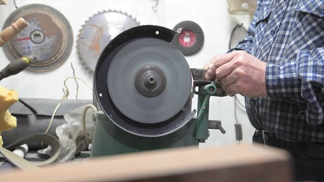 A desktop metal sharpening and grinding machine is in operation. Working hands sharpen a metal part on a desktop electric grinding machine