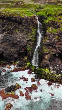 Volcanic cliff Azores with waterfall flowing into Atlantic ocean water, rugged Atlantic coast landscape of Azores island