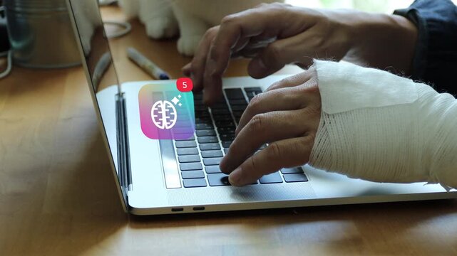 Injured East Asian man with a bandaged hand typing on laptop keyboard, showing a 3D tracked glowing brain top view creative AI notification pop up and red counter.