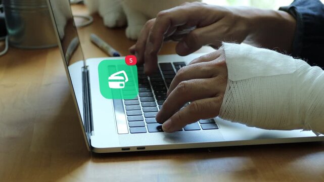 Injured East Asian man with a bandaged hand typing on laptop keyboard, featuring a 3D tracked credit card electronic payment banking notification pop up and red counter.