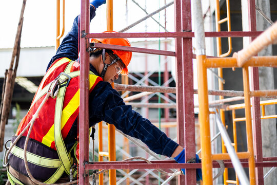 Construction worker wearing a safety harness while working on scaffolding at a building site.