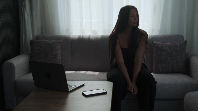 Mental block and indecision concept with young woman struggling to start work while sitting on sofa at home, anxiety and procrastination behavior