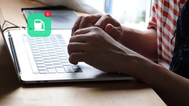 Casual Asian man hands typing on a laptop computer keyboard, with a 3D tracked fuel gas station location pointer map notification pop up and red counter.