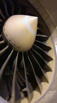 Dramatic low angle tilt shot focusing on commercial jet engine fan blades spinning with glossy golden metal textures inside an airport hangar maintenance bay