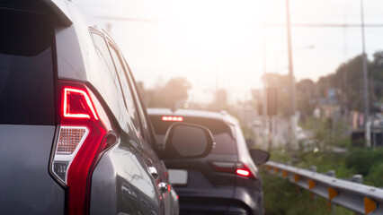 Vehicles are gridlocked in a heavy urban traffic jam during a bright afternoon. A silver SUV's glowing red tail light assembly stands out sharply in the foreground lane. © thongchainak