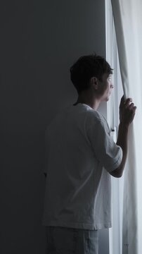Social anxiety and isolation concept with introvert person cautiously looking through curtain, loneliness, emotional stress and mental discomfort atmosphere, vertical video