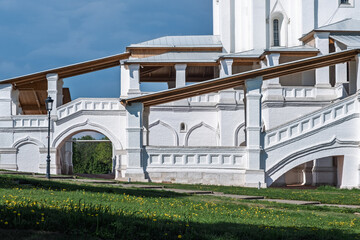 Naklejka premium Architectural features of a historic white structure with arched walkways and wooden roofs, set against a blue sky and green grass