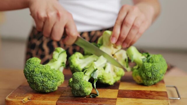 A person is cutting fresh broccoli on a wooden cutting board. The kitchen has a warm feel as food is being prepared for a meal