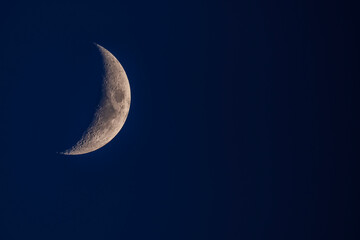 Vertical macro shot of a golden waxing crescent moon on a dark navy blue night sky background. © underwaterstas