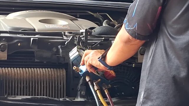 Professional auto mechanic calmly inspecting and servicing a vehicle air conditioning system in a modern, well-equipped auto repair garage.