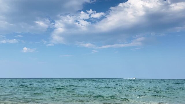 Timelapse clouds racing across blue sky above calm sea. Distant yacht moving along ocean horizon, cloud movement over seascape, blue water, marine landscape and open horizon.