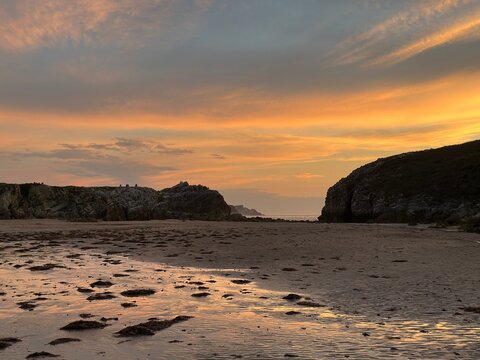 Warm evening sky reflected across rippled wet sand exposed by low tide between coastal rock formations.
