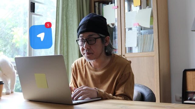 Long white haired mature Asian man with glasses using laptop at home office, with a 3D tracked location pointer navigation arrow map notification pop up and red counter.