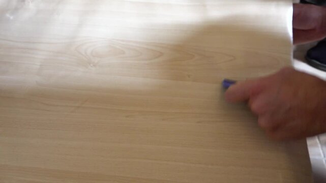 Close up view of a person using a squeegee to apply self-adhesive vinyl film onto a cabinet surface under a sink during home renovation.