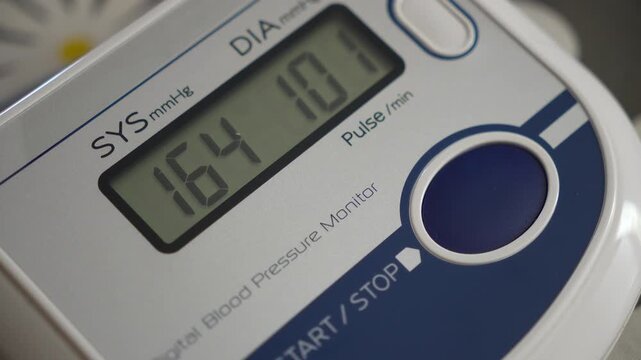 Macro shot of a digital blood pressure monitor display showing high hypertension and pulse readings.