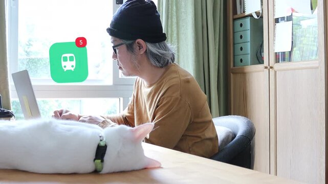 Side view of a mature Asian man using a laptop at home office next to his cat, featuring a 3D tracked skytrain subway transit notification pop up and red counter.