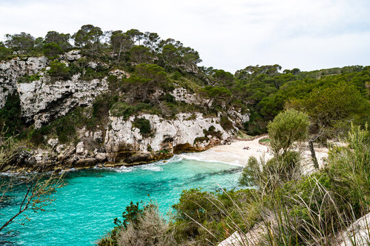 Stunning horizontal view of a hidden Mediterranean cove in Menorca with vibrant turquoise water, sandy beach, and limestone cliffs