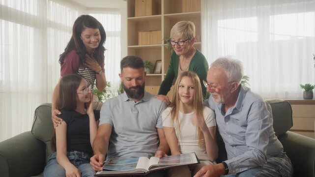 Happy multigenerational family with wife, daughters and grandparents looking at photo album at home