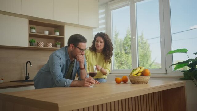 Young couple boyfriend and girlfriend fighting shouting arguing at home kitchen. Alcohol addicted man drinking wine. Family quarrel, addiction issue.