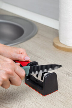 A woman sharpens a knife in the kitchen, vertical photo. knife sharpening process. home knife sharpener. manual sharpener for a kitchen knife. Vertical photo