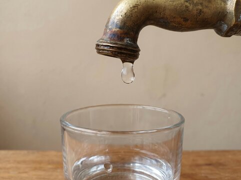 Water Scarcity: A Single Drop Hanging From an Old Dry Tap Above an Almost Empty Glass