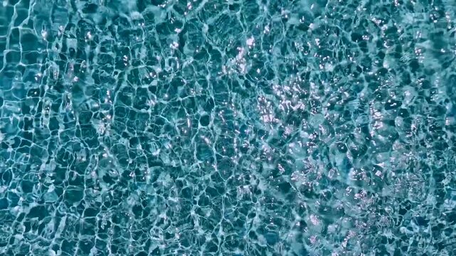 Full frame overhead view of crystal clear turquoise swimming pool water with bright sparkling sun glares and ripples
