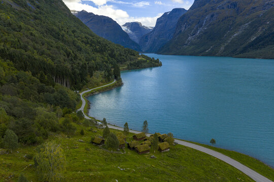 Aerial view of the historic Breng seter farm with traditional grass-roofed cabins on the banks of the turquoise Lake Lovatnet in Stryn Municipality, Vestland, Norway.