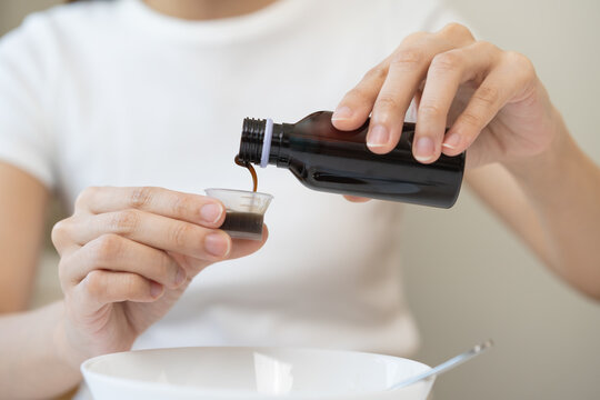 Close up hand of sick woman pouring syrup, liquid antipyretic, cough, flu medicine to jar from bottle, measuring dosage of drug with cup, taking therapy, treatment cure of disease. Health care concept