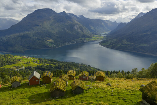 Aerial view of Rakssetra with traditional grass-roofed wooden cabins overlooking the deep blue waters of the fjord and surrounding mountains in Stryn Municipality, Vestland, Norway.