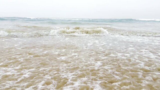 Bright ocean waves gently washing over a sandy tropical beach in sunlight, peaceful coastal seascape with turquoise water, white sea foam and relaxing summer vacation atmosphere in 4K slow motion