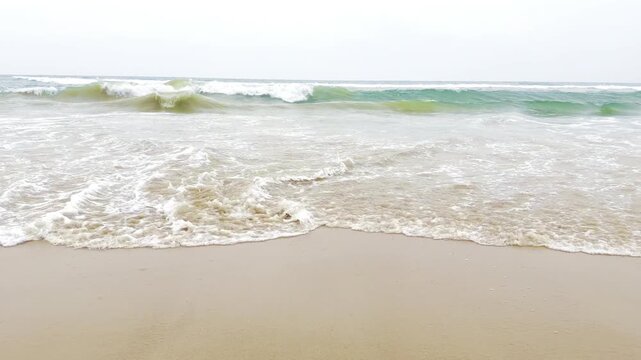 Bright ocean waves gently washing over a sandy tropical beach in sunlight, peaceful coastal seascape with turquoise water, white sea foam and relaxing summer vacation atmosphere in 4K slow motion