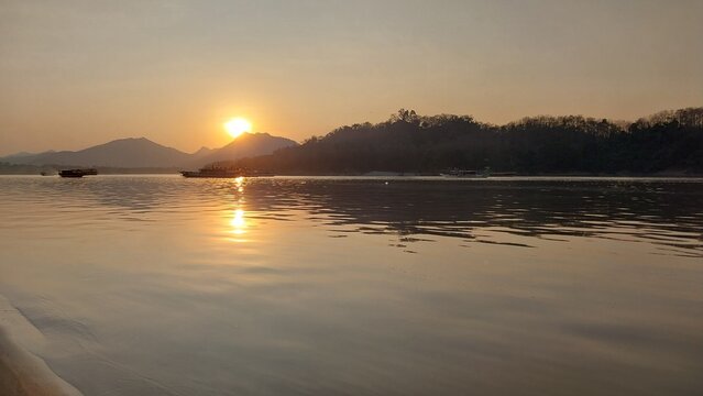 Serene sunset over a calm river, reflecting warm hues with silhouettes of distant mountains.